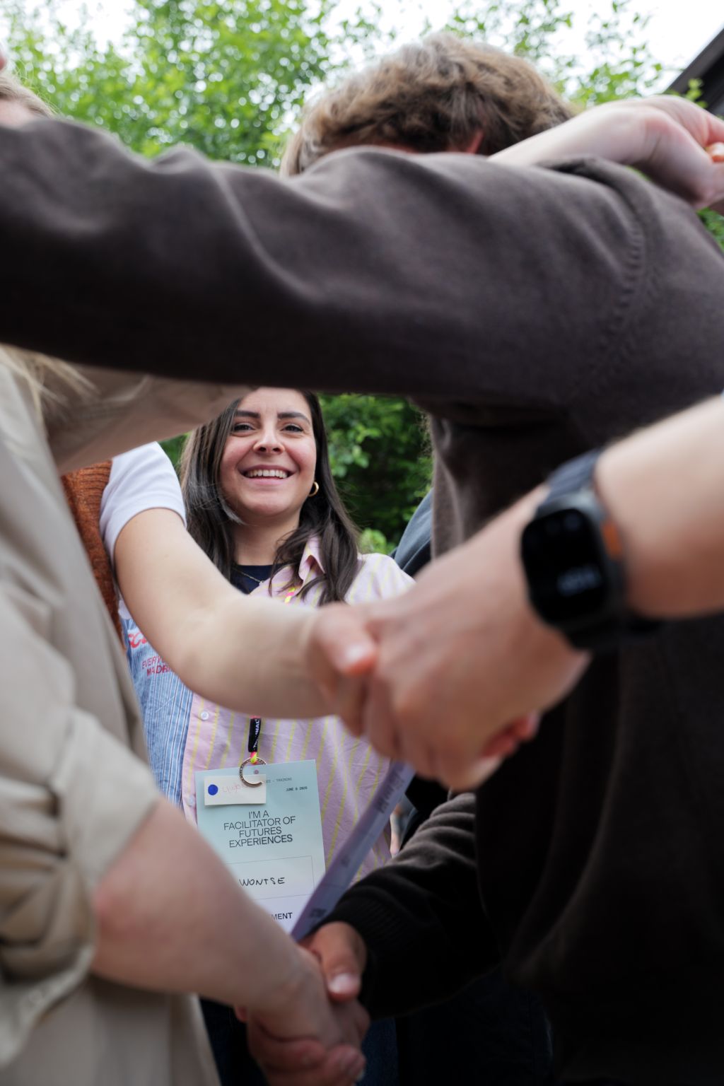 A participant smiling amid a circle of linking arms and handshakes outdoors
