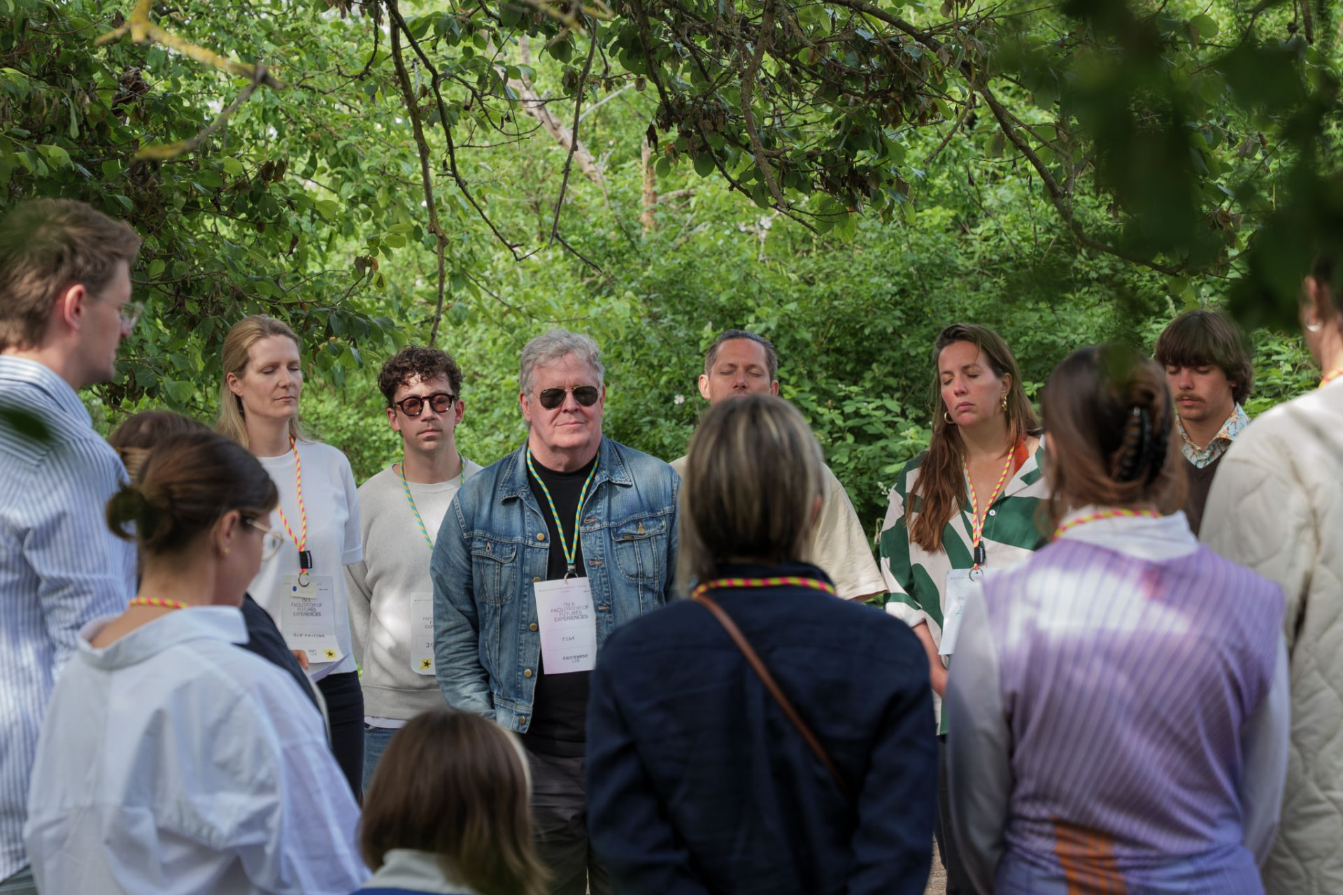 A circle of participants standing together in a lush green wooded setting